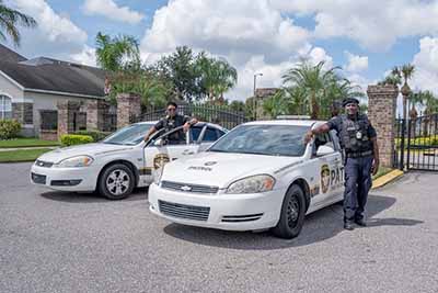 Two security patrol officers standing beside marked patrol vehicles at a gated community in Orlando, Florida.