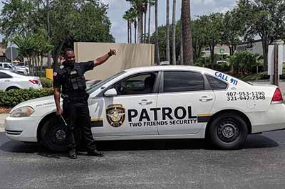 A security guard from Two Friends Security LLC standing next to a marked patrol vehicle in Orlando, Florida.